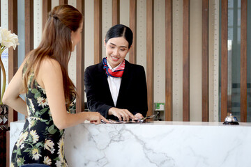 Beautiful smiling Asian receptionist suggests travel program for tourist woman customer, female...