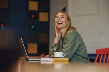 Smiling businesswoman working on laptop in modern coworking. Distance work concept