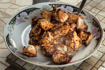 Tender and juicy chicken skewers cooked on coals in an open grill are laid out on a dish. Delicious kebab or barbecue