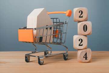 Stacked wooden blocks with 2024 numbers and a cart inside with a wooden house, home sale target...
