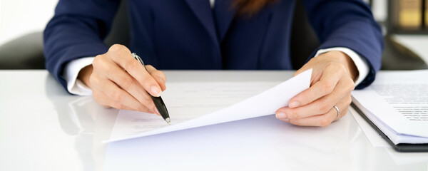 Business woman lawyer executive wearing suit holding pen in hand writing in notebook or contract legal financial document, filling insurance form, taking notes, putting signature in corporate papers.