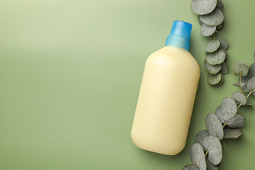 Bottle of fabric softener and eucalyptus leaves on light green background, flat lay. Space for text