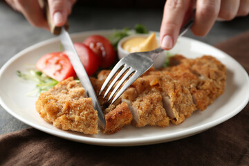 Woman eating delicious schnitzel at table, closeup