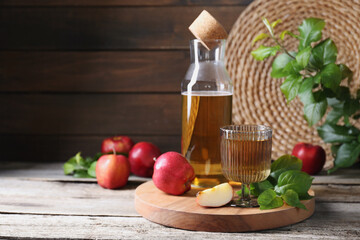 Delicious cider and apples with green leaves on wooden table, space for text