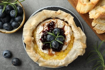 Tasty baked brie cheese with blueberries, jam and rosemary on grey table, flat lay