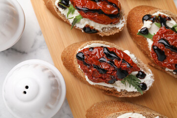 Delicious bruschettas with sun-dried tomatoes, cream cheese and balsamic vinegar on white table, flat lay