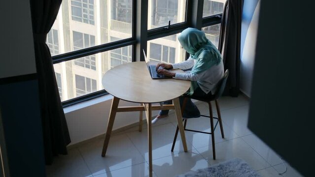 Witness a skilled Muslim woman, adorned in her hijab, engaging in remote work from the comfort of her home, symbolizing the seamless blend of telecommuting, technology, cultural diversity, and empower