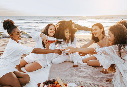 Summer picnic at sunset. Group of happy diverse women pouring champagne in glasses, having bachelorette party - Powered by Adobe