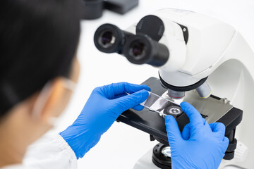 Scientist hands wearing blue gloves holding glasses slide for diagnosis hematology.Microscopy background at laboratory.Scientist doing some research.Medical technician analysis blood slide.