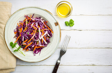 Fresh coleslaw salad made of shredded red and white cabbage and carrots on white wooden background, top view