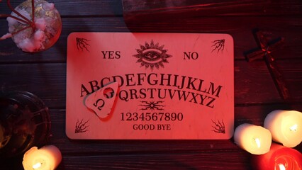 Close up shot of a wooden ouija board with a planchette on a table surrounded by candles,...