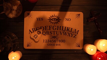 Close up shot of a wooden ouija board with a planchette on a table surrounded by candles,...