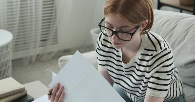 Confident Caucasian teenage girl is depicted diligently working on her homework at home. The scene captures her self-assured and focused demeanor as she tackles her academic tasks.