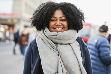 Young african woman smiling on camera at bus station in the city during winter time