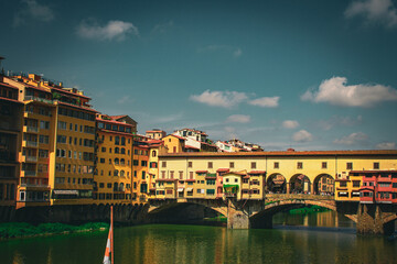 The Ponte Vecchio stretches across the Arno River in Florence, its vibrant shops and houses reflecting in the water, an emblem of Renaissance beauty and bustling city life.