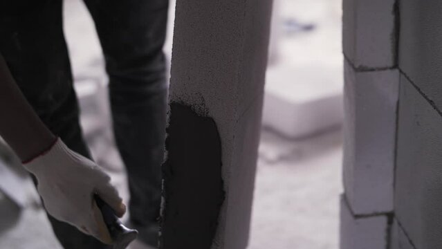 A worker applies concrete mortar to a brick
