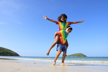 Lesbian woman on back ride with partner laughing in joy and happiness by the beach ,lesbian, and a couple at the beach and piggyback ride for love, summer and vacation together for LGBTQ, travel, and 