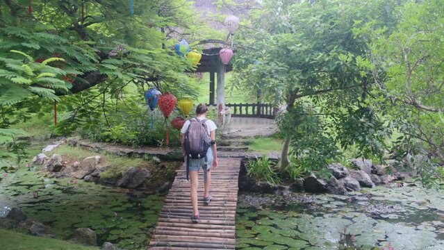 Young woman explores a natural park in Vietnam amidst vibrant traditional Vietnamese lanterns hanging from trees. A colorful contrast in a natural setting, blending culture, and nature. Woman discover