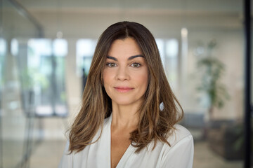 Confident smiling Latin professional mid aged elegant business woman corporate leader, happy beautiful mature female executive, lady manager standing in office looking at camera, headshot portrait. - obrazy, fototapety, plakaty