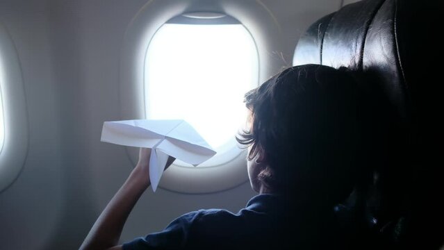 Child plays with a paper airplane inside an airplane looking out the window. Concept of imagination, travel with children and adventure of growing up