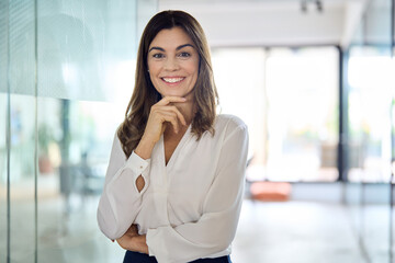 Happy confident Latin professional mid aged business woman in office, portrait. Smiling lady corporate leader, mature female executive, lady manager standing in looking at camera, portrait.