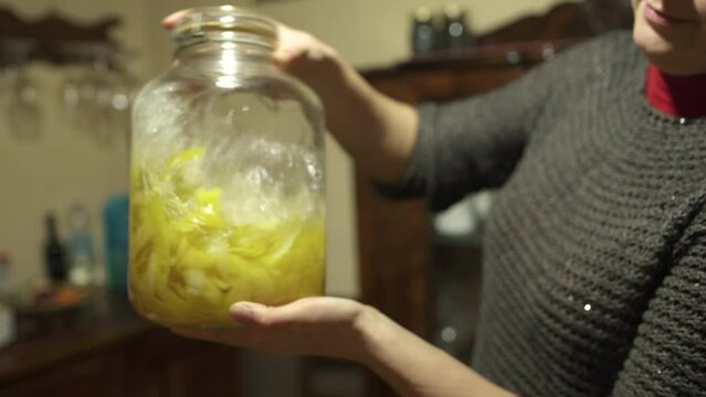 Homemade alcoholic drink limoncello in the home kitchen in the Italian village. Woman mixing lemon peel with alcohol in the jar 4K