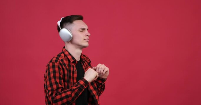 Caucasian man on a red background embraces the power of music. With his headphones on and a wide smile adorning face, he moves effortlessly to the rhythm, allowing the beats to guide his every step.