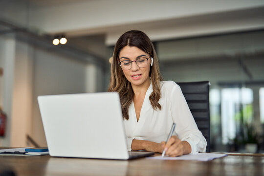 Busy mature business woman corporate leader, company team leader executive, hr manager having hybrid conference call meeting or remote online job interview on laptop computer working in office.