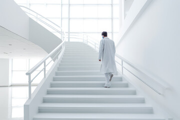 Doctor moving down from staircase in hospital. All white clean hospital environment.