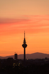 Obraz premium Silhouettes of buildings of a city, highlighting the silhouette of a communications tower with an orange sky with clouds at sunset