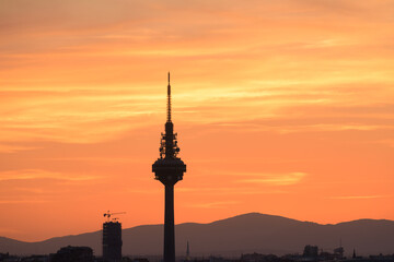 Obraz premium Silhouettes of buildings of a city, highlighting the silhouette of a communications tower with an orange sky with clouds at sunset