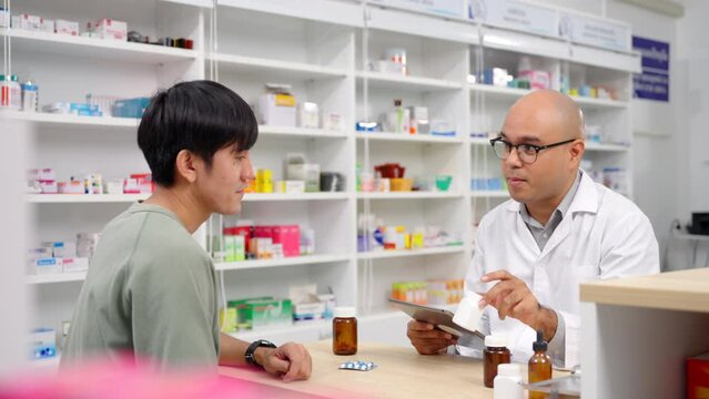 Handsome asian male pharmacist analyzing about customer symptoms for discussion of the medicine property effect with tablet and customer buying pill under prescription order. 4k resolution.