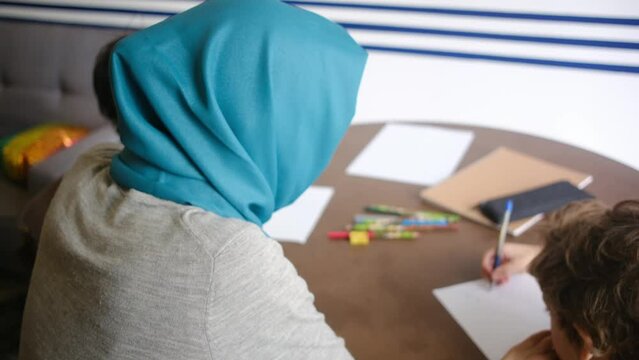 Embrace the world of learning and love with our heartwarming.Witness a Muslim mother in a hijab guiding her 6 and 8-year-old children through their school tasks at home, blending educatio  family.