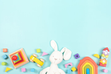 Baby kids toy frame background. White bunny, colorful wooden educational, sensory, sorting and stacking toys for children on light blue background. Top view, flat lay