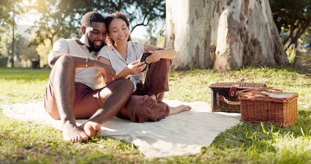 Happy, social media and an interracial couple on a picnic with a phone for communication, tech or...
