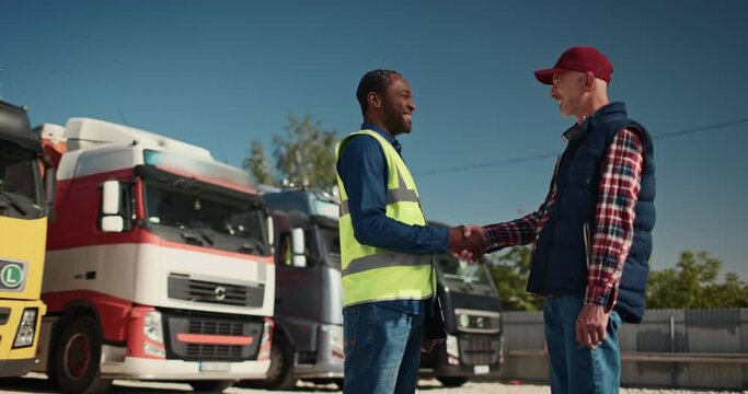 Truck driver talking to shipment supervisor and shaking hands. Two employees standing in front of big truck. Workers talking and perform technical inspection of vehicle before next drive.