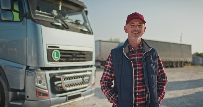 Portrait of lorry driver standing in front of truck after successfully completed tour. Confident truck driver with his vehicle in parking lot. Truck car travels, transportation and delivery.
