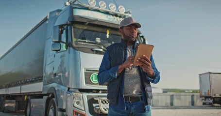 African American professional truck driver setting up navigation for destination. Checking his route on tablet computer and standing by long vehicle. Transportation service.