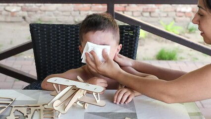 Little boy sneezing or blowing his nose with mother helping hands. Wrinkled nose, squinted eyes, ill baby in family. Flu, runny nose, virus or allergy concept.