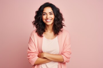 Fototapeta premium Portrait of a smiling young woman standing with arms crossed against pink background