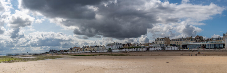 Fototapeta na wymiar Luc-Sur-Mer, France, France - 07 26 2023: View of a cloudy rainy sky, the wooden Fisherman's Pier, the seawall, beach cabins and people above the sea from the beach.