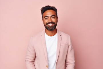 Fototapeta premium Portrait of a handsome young Indian man smiling at the camera while standing against pink background