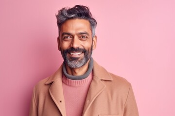 Obraz premium Portrait of a handsome Indian man with gray hair and beard wearing beige coat and smiling at the camera while standing against pink background