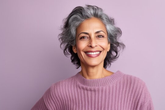 Lifestyle portrait of an Indian woman in her 50s against a pastel or soft colors background wearing a cozy sweater