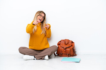 Uruguayan student woman sitting one the floor isolated on white background pointing to the front and smiling