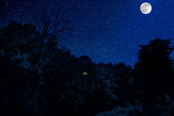 Mountain night landscape of building at forest at night with moon or vintage country house at night with clouds and stars. Summer night.