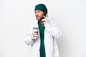 Middle age surgeon in green uniform isolated on white background holding coffee to take away and a mobile