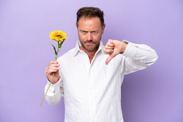 Middle age caucasian man holding sun flower isolated on purple background showing thumb down with...