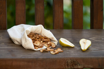 Pear potato chips in a natural fabric bag on a wooden table with wood texture on a green garden background in the background. Nearby a ripe pear cut in half.