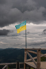 The Ukrainian flag on the top of a mountain on the background of dark clouds, Carpathian mountains